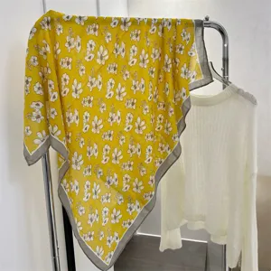 Detail view of a 90cm yellow floral cotton linen square scarf on a clothing rack