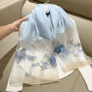 Detailed view of an elegant light blue silk blend scarf with blue floral embroidery.