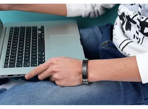 Lifestyle detail of a men's stainless steel mesh bracelet worn while using a modern laptop