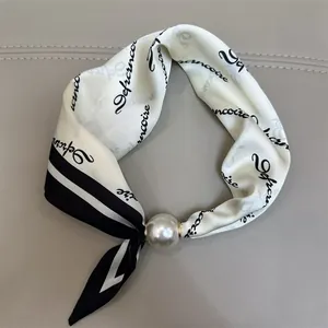 Elegante witte zijden sjaal met zwarte print en een grote parelgesp accessoire