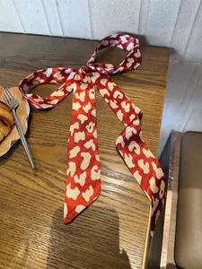 Rode en witte zijden sjaal met koeienprint als haarstrik op een houten tafel