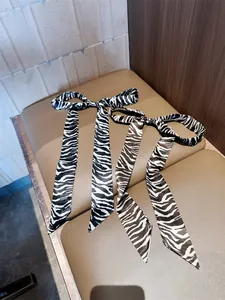 Close-up van smalle sjaals met zebraprint in zwart en bruin gestrikt op een leren zitting.