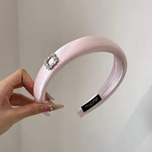 Nahaufnahme eines gepolsterten rosa Satin-Haarreifs mit quadratischer Strass-Schnalle.