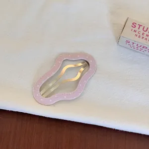Détail d'une pince à cheveux BB rose à pois en forme de nuage sur un tissu blanc doux.