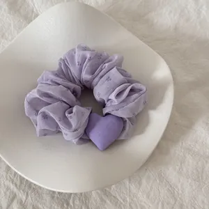 Λεπτομέρεια από μωβ λουλουδάτο scrunchie με καρδιά σε κομψό λευκό πιάτο.