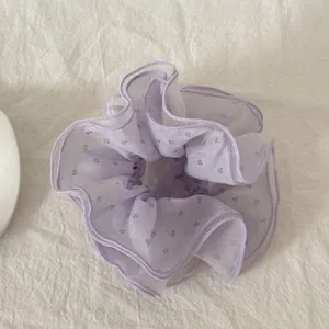 Λεπτομερής άποψη από μωβ λουλουδάτο scrunchie με κομψά βολάν σε λευκό λινό ύφασμα