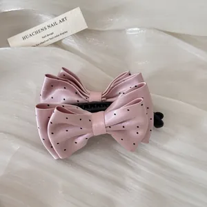Detailed view of a pink satin polka dot bow hair comb hair accessory on white fabric