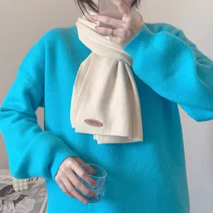 Detailansicht eines weichen cremefarbenen minimalistischen Strickschals über einem Pullover