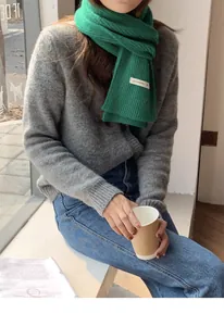 Primo piano di una sciarpa in maglia a coste verde su una modella in un set accogliente