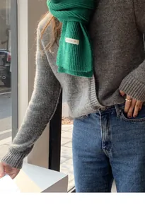 Sciarpa in maglia verde per l'inverno con un dettaglio di etichetta minimalista.