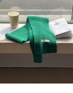 Dettaglio di una sciarpa a maglia verde con trama a coste e etichetta decorativa in tessuto.