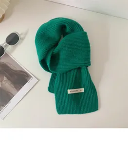 Dettaglio di una sciarpa corta a coste verde acceso con un'etichetta bianca decorativa.