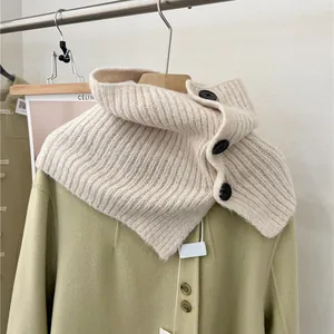 Detail of a beige knitted neck warmer with three black buttons and soft rib texture