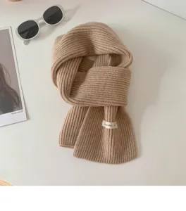 Dettaglio di una morbida sciarpa corta in maglia beige con piccola etichetta bianca