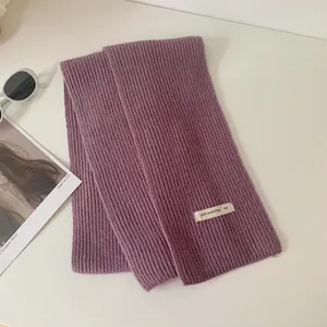 Dettaglio di sciarpa in maglia viola con etichetta 'girls need stley, too'.