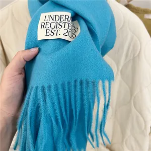 Close-up of a vibrant blue faux cashmere scarf with fringe and a white text label detail.