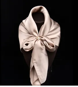 Nahaufnahme eines eleganten goldenen X-förmigen Schalrings auf Seide