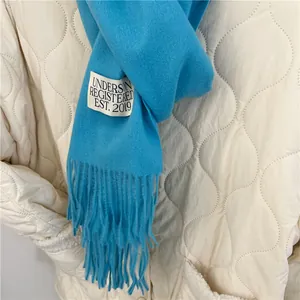 Close-up detail of a soft blue imitation cashmere scarf featuring fringe and a sewn tag