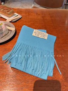 Detail view of a soft sky blue cashmere-like scarf with fringe tassels and brand label
