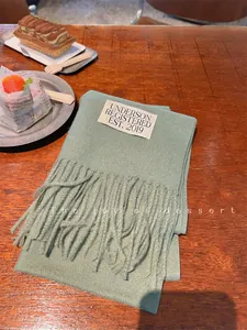 Detailed close-up of a soft sage green faux cashmere scarf featuring elegant fringes