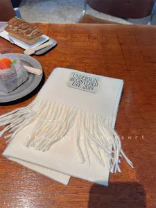 Close-up of a soft cream faux cashmere scarf with elegant fringe and brand label