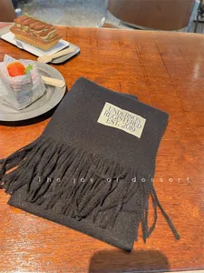 Detailed shot of a black faux cashmere scarf with tassels and label on a wooden table