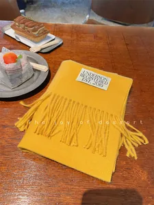 Detail of a soft yellow imitation cashmere scarf with decorative tassels and label