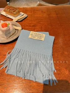 Close-up detail of a soft blue winter scarf with fringe tassels on a wooden surface.