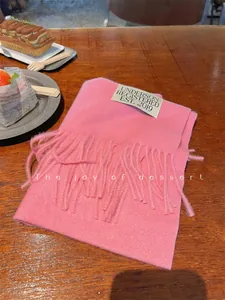 Cozy pink faux cashmere scarf with tassels on a wooden cafe table.