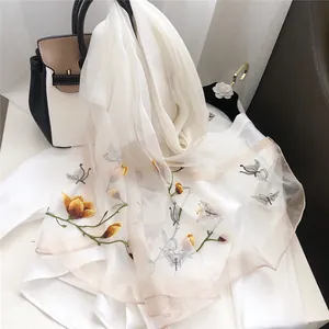 Close-up of elegant embroidered silk scarf with yellow flowers and butterfly details.