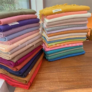 Neatly stacked colorful soft solid winter scarves with fringe tassels displayed on wood