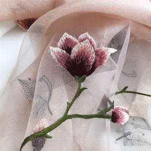 Elegant close-up showing detailed magnolia and butterfly embroidery on a pink silk scarf