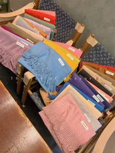 Detailed view of various colorful solid scarves with elegant tassels and small fabric labels.