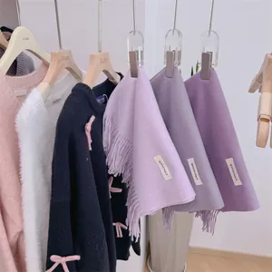 Close-up detail of soft smoky purple knit scarves with fringe hanging on a clothing rack.