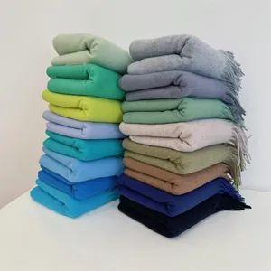 Stack of soft winter shawls in various solid colors with fringe and tassel details