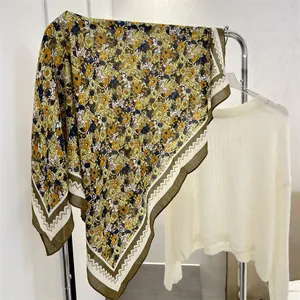 Detailed view of a yellow floral cotton linen scarf hanging on a rack with a sweater
