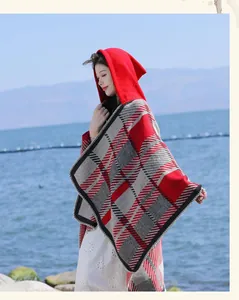 Side view of woman in red plaid hooded poncho against a scenic blue lakeside backdrop