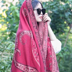 Detail view of a thick red ethnic paisley shawl wrap worn by a model in nature