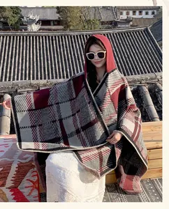 Asian woman wearing a stylish red and grey plaid hooded cloak shawl in a retro scenic setting.