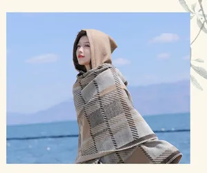 Close-up of a vintage plaid hooded shawl cloak worn by a model against sea background.