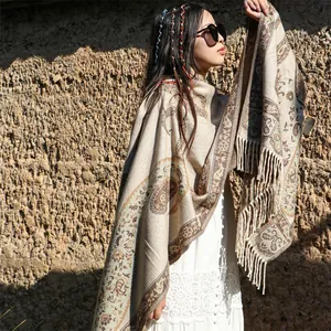 Woman wearing an ethnic paisley shawl with tassels in front of a rustic mud wall