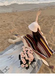 Rückansicht eines Modells mit buntem ethnischen Strickponcho an einem Sandstrand bei Sonnenuntergang