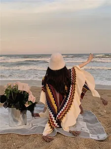 Detailansicht eines farbenfrohen Ethno-Ponchos mit Fransen am Strand bei Sonnenuntergang