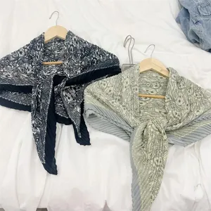 Two pleated square scarves with paisley patterns on wooden hangers against white fabric