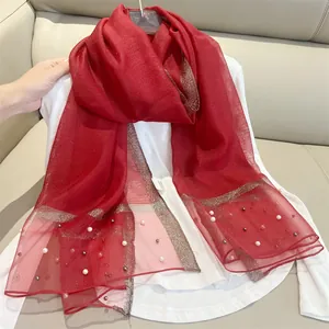 Close-up detail of elegant red silk-like scarf with pearl accents and metallic edging.