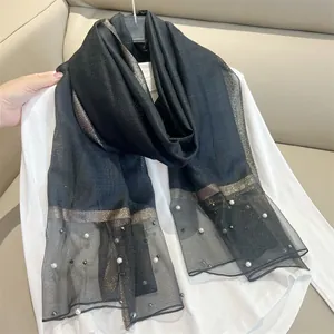 Detail shot of black faux silk scarf featuring pearl accents and gold metallic trim.