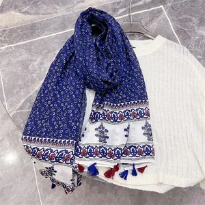Detail view of an ethnic style tassel scarf with blue floral prints on a white sweater.