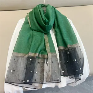 Detail view of a green silk scarf with elegant pearls and black mesh trim design.