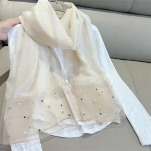 Detail view of off-white faux silk scarf with elegant pearl embellishments on mesh ends.