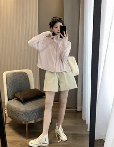 Modella asiatica con un'elegante giacca protettiva UV rosa cipria dal taglio a mantella con cappuccio.